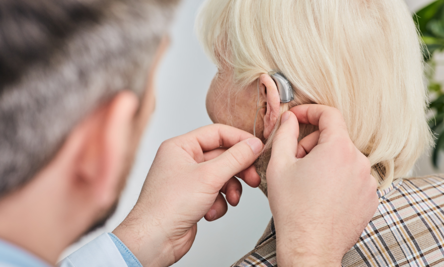 Audiologist fits hearing aid into senior woman's ear