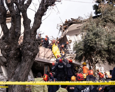 Istanbul first responders standing on top of a wrecked house and rubble handing off a deceased person in a body bag to other first responders on the ground