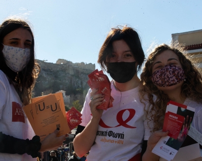 Three female volunteers, wearing cloth face masks, pose with leaflets about sexual health in Athens, Greece, on World AIDS Day, Dec. 1, 2021.